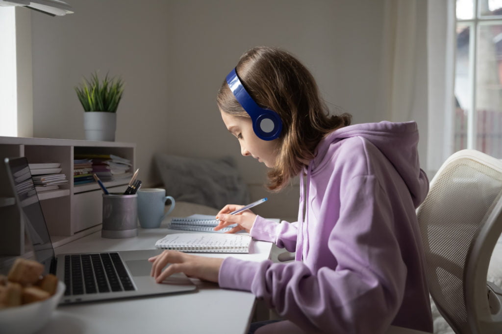 Teen Girl With Headphones Studying Online and Taking Notes