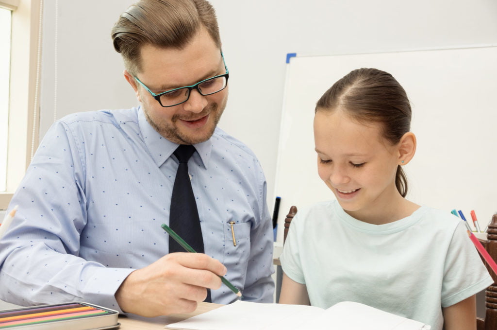 Young teacher and schoolgirl writing in classroom